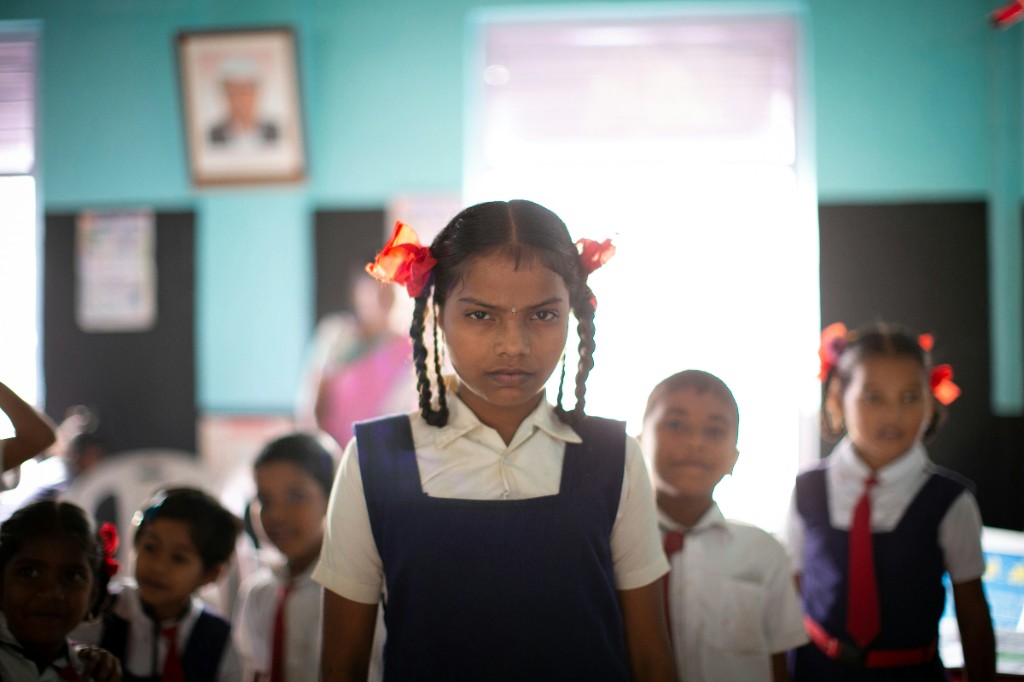 A schoolgirl in uniform looking at the camera in a bright classroom