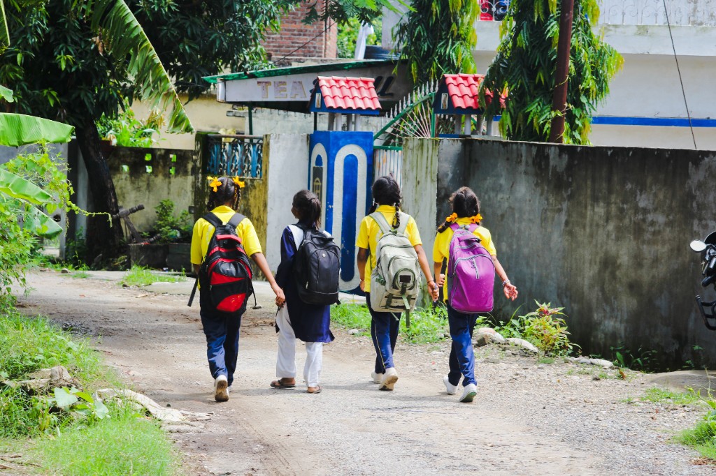Four schoolgirls walking together down a path with backpacks