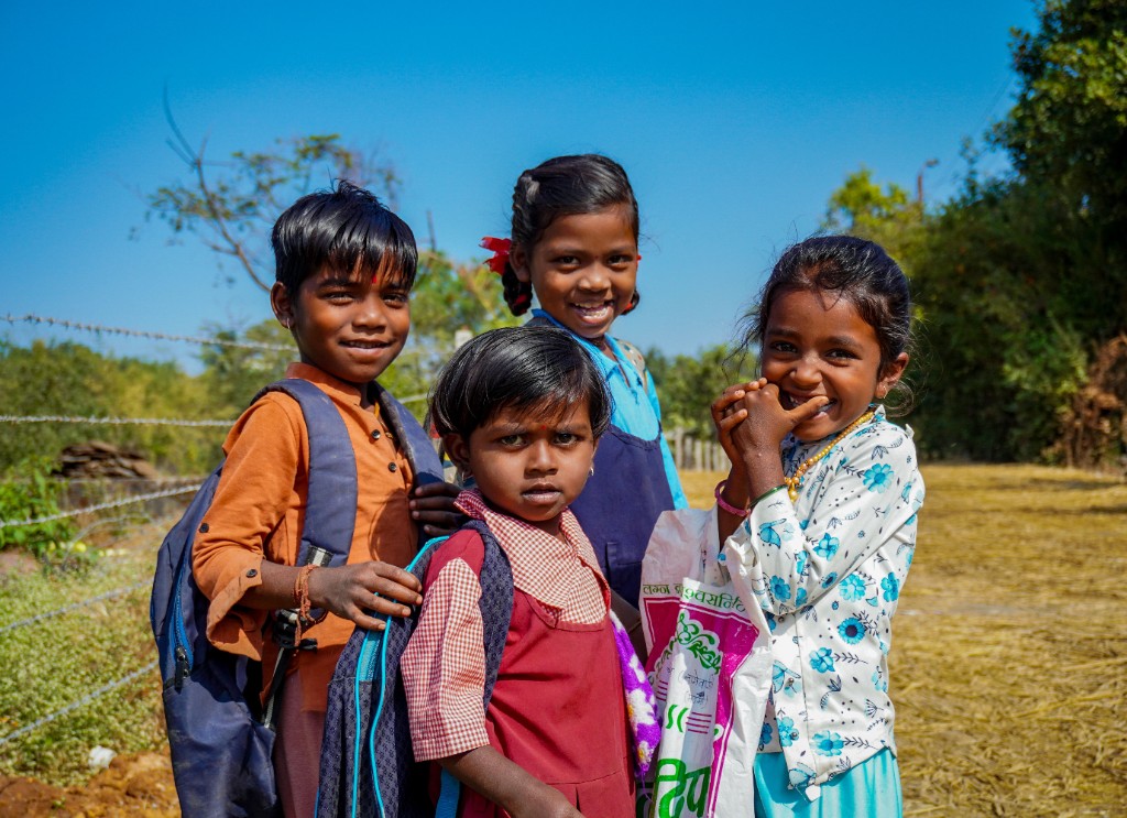 Four children smiling outdoors under a clear blue sky